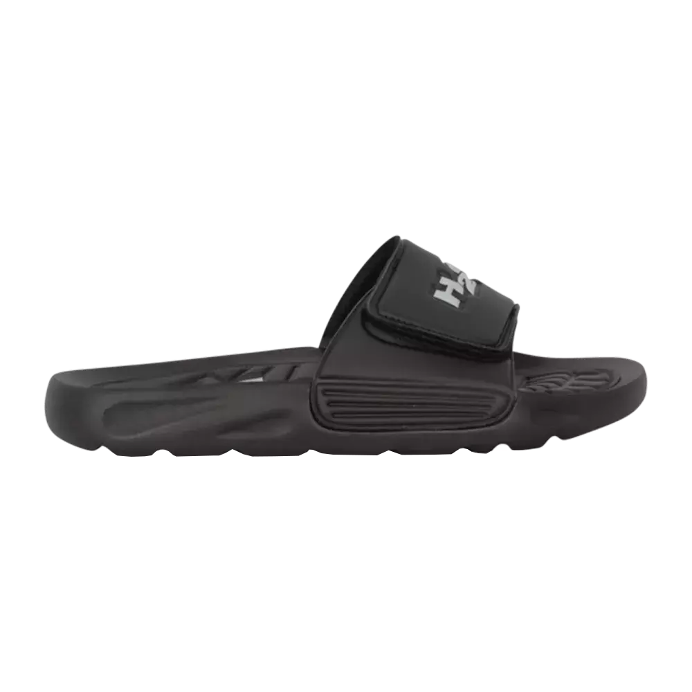 En enkel, sort badesandal med bred, justerbar rem og velcrolukning. Skoens sål er formstøbt og har en blød, polstret profil med mønstret fodbed for bedre greb. Remmen er let polstret og prydet med et diskret logo. Sandalen har et robust, skridsikkert ydersål og et minimalistisk design, der gør den praktisk til pool, strand eller afslappet hverdag.