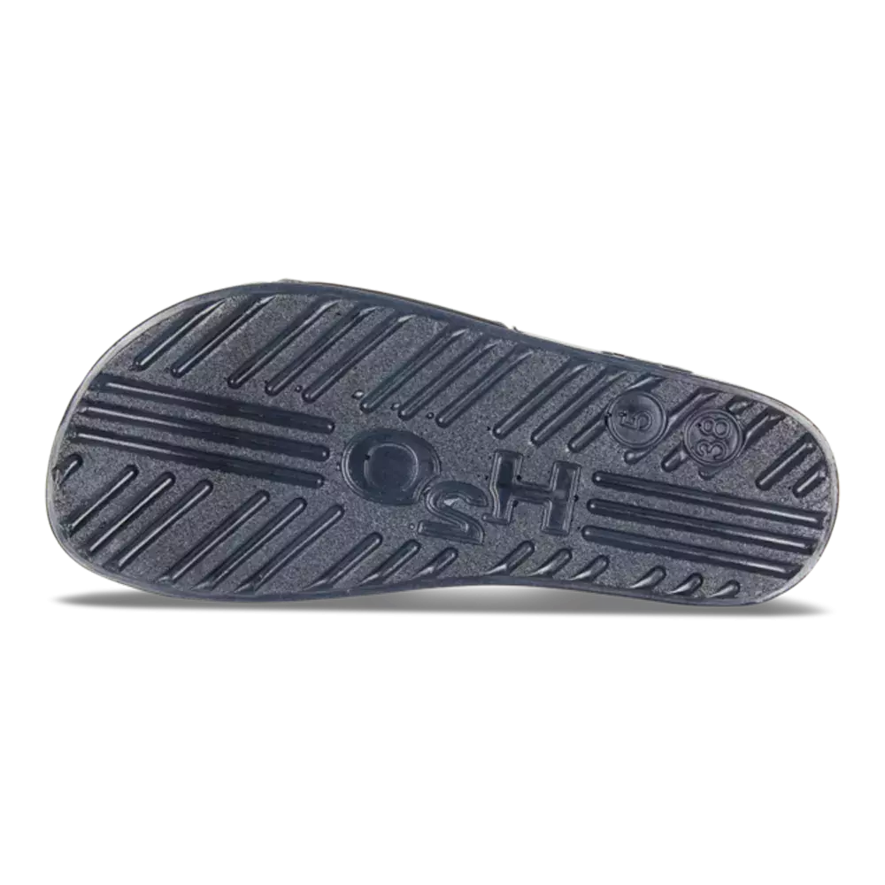 På billedet ses sålen af en sko set fra undersiden. Mørk gummisål med skrå rillemønstre, tværgående lameller og flere runde aftryk for ekstra greb. Et lettere forhøjet midtpunkt og præget tekst fremtræder i midten, samt en indstøbt størrelsesmarkering ved hælen. Sålen virker robust og let brugt, designet til at give holdbarhed og skridsikkerhed i hverdagssituationer.