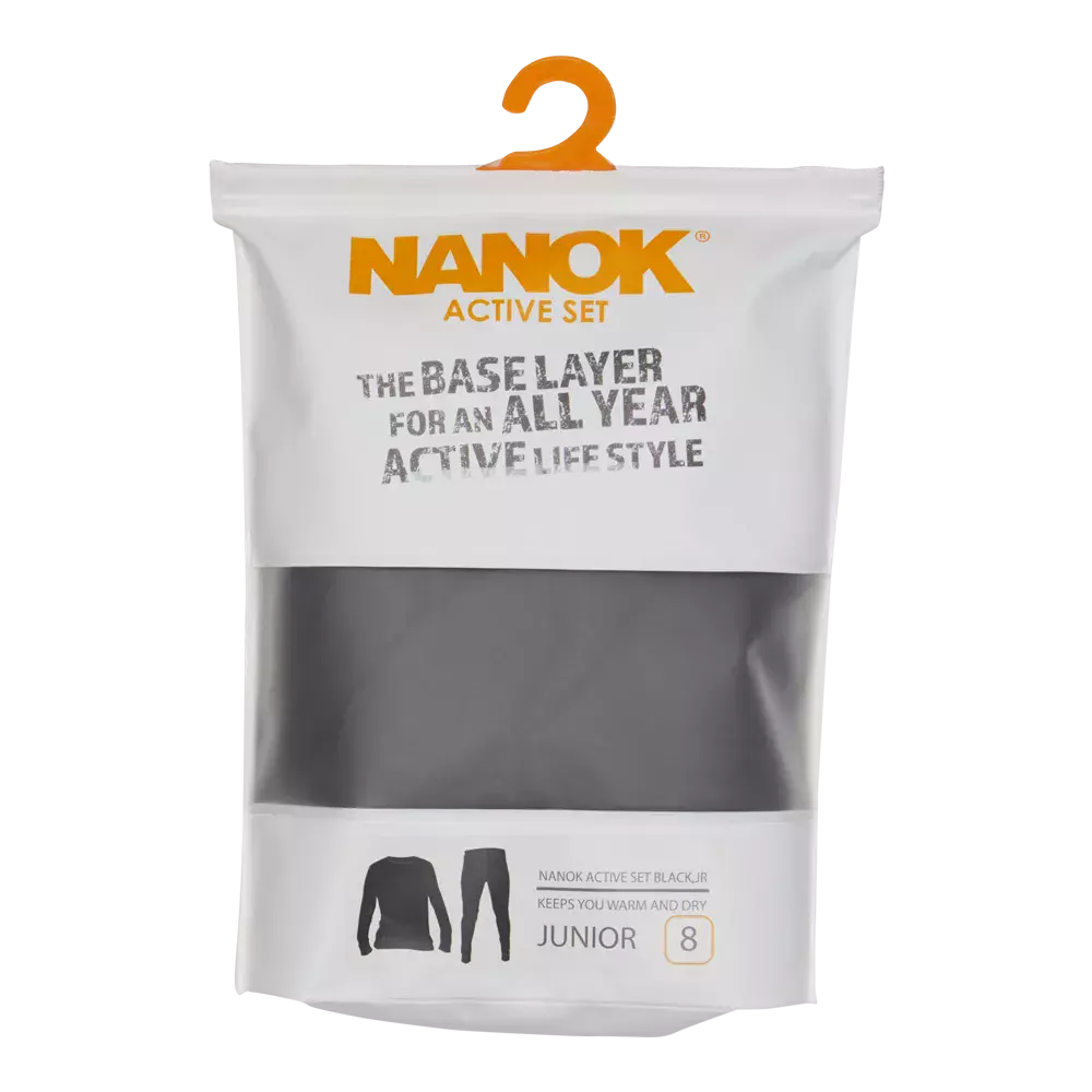 Et foto af en forpakning til NANOK Active Set i juniorstørrelse. Den hvide emballage har en tydelig orange NANOK‑logo øverst og teksten "The base layer for an all year active lifestyle". Gennem et gennemsigtigt vindue ses det sorte undertøjsstof. Nederst er silhouetter af trøje og buks, mærket "Junior" og størrelse 8. Pakningen har også en orange bøjle til ophæng i butikken.