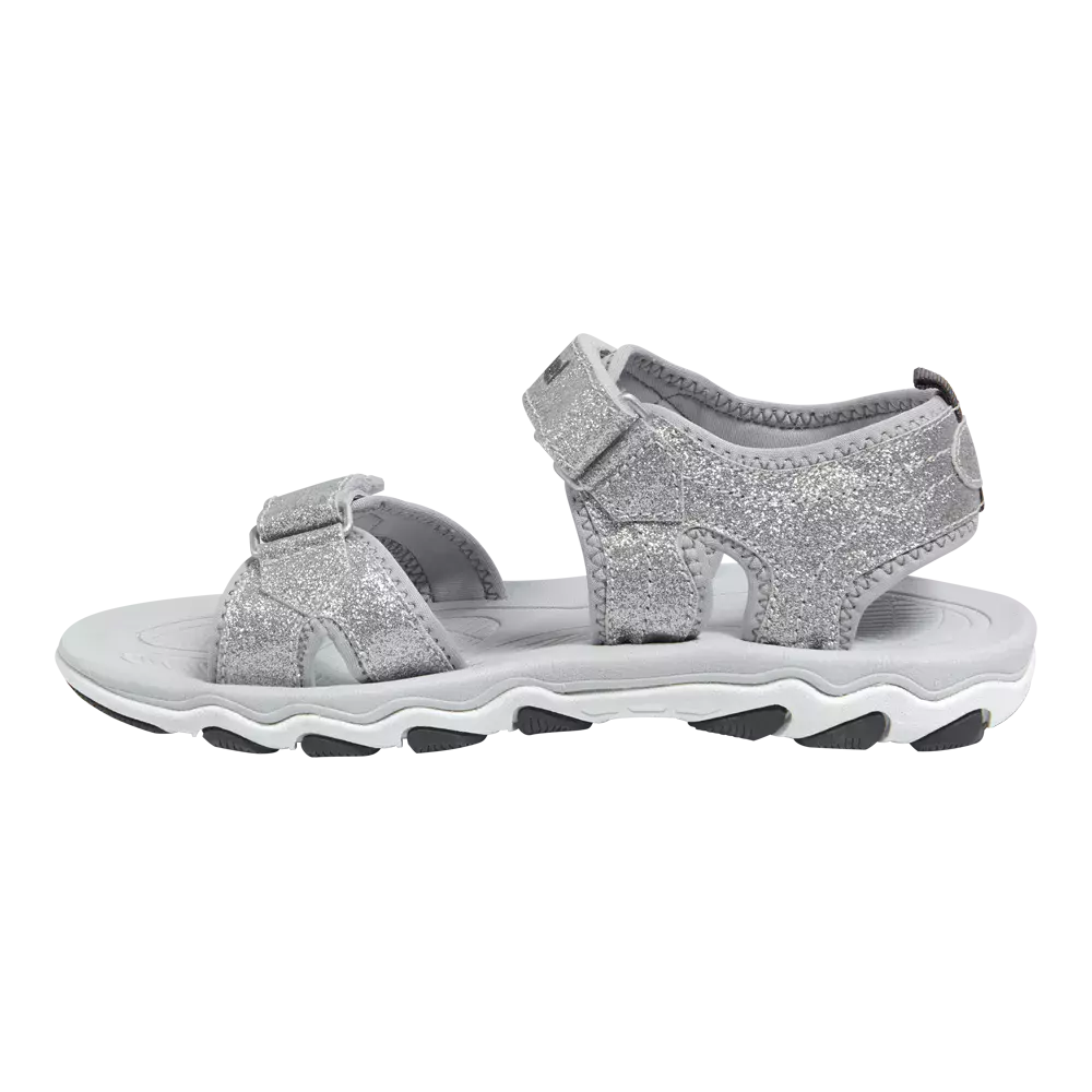 En sølvglitrende børnesandal med åbne tå- og hælkonstruktion, lavet med bløde, polstrede stropper og praktiske velcro-lukninger for justerbar pasform. Overfladen er dækket af fint glitter, mens indersålen virker polstret for komfort. Den robuste, bølgede gummisål i hvid og grå giver godt greb og stødabsorbering. Sandalen passer til både hverdag og festlige sommerlejligheder, hvor holdbarhed kombineres med et funklende look.
