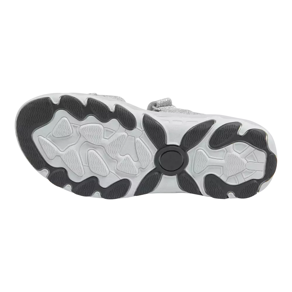 På billedet ses sålen af en sportssko set skråt nedefra. Vibram-lignende slidbane i hvidt gummi med mørkegrå gummipuder ved kontaktpunkter, bølgede mønstre og dybe riller for fleksibilitet og greb. Midtunder er en rund, forstærket drejezone, mens små teksturerede felter øger friktionen. Sålen virker robust og designet til daglig brug og god affjedring, med fokus på stabilitet og skridsikkerhed.