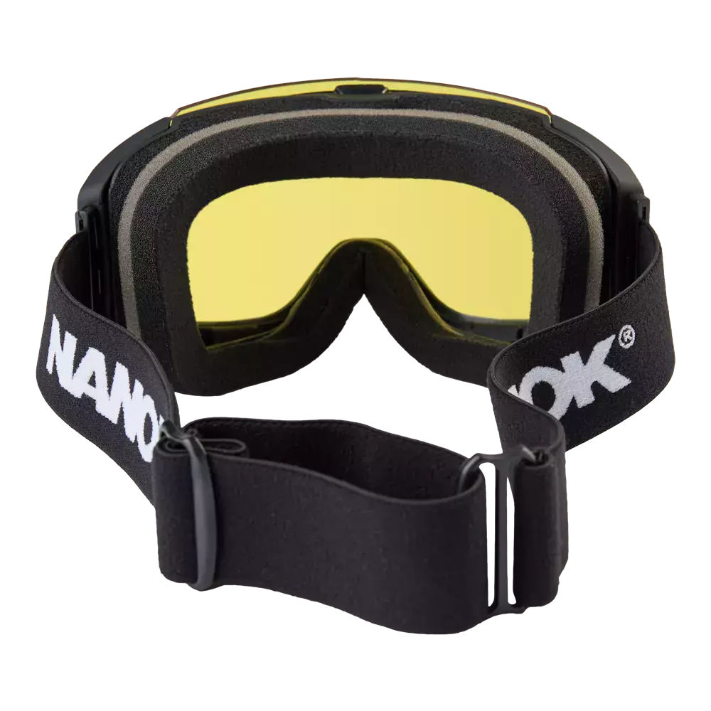 goggles med sort stel og klar gultonet linse. Indersiden har blød, lagdelt skumgummi for komfort og tætning mod vind og sne. Brillen har en bred, elastisk sort strop med hvidt logo og justerbar spænde, så den sidder fast omkring hjelmen. Designet virker robust og funktionelt, velegnet til udendørs aktiviteter i koldt vejr.