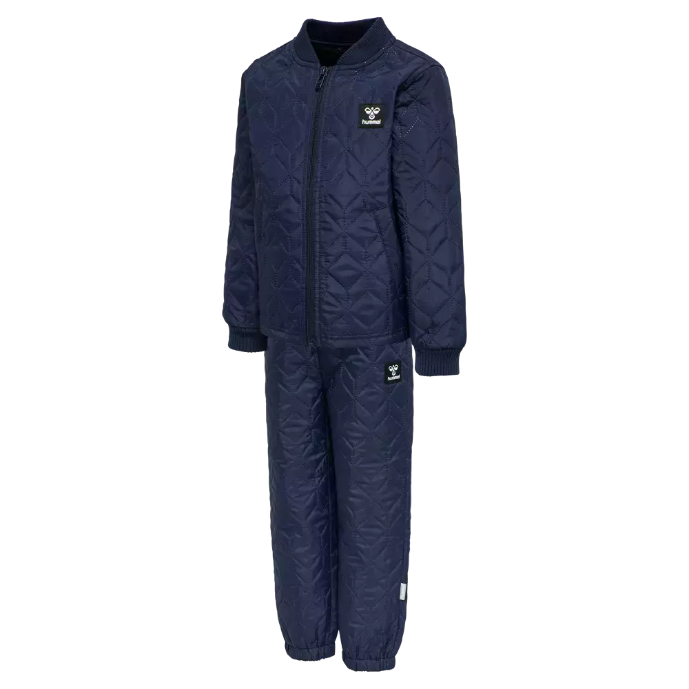 Et mørkeblå, quiltet to-delt sæt bestående af en lynlåstrøje og matchende bukser. Jakken har en rund ribkrave, lange ærmer med ribmanchetter og en fuld lynlås foran, mens bukserne har elastiske ankler for bedre pasform. Stoffet er let vatteret med diskret diamantmønster, og små logo-patches på bryst og lår giver et sporty og enkelt udtryk. Komfortabelt og praktisk til kølige dage.