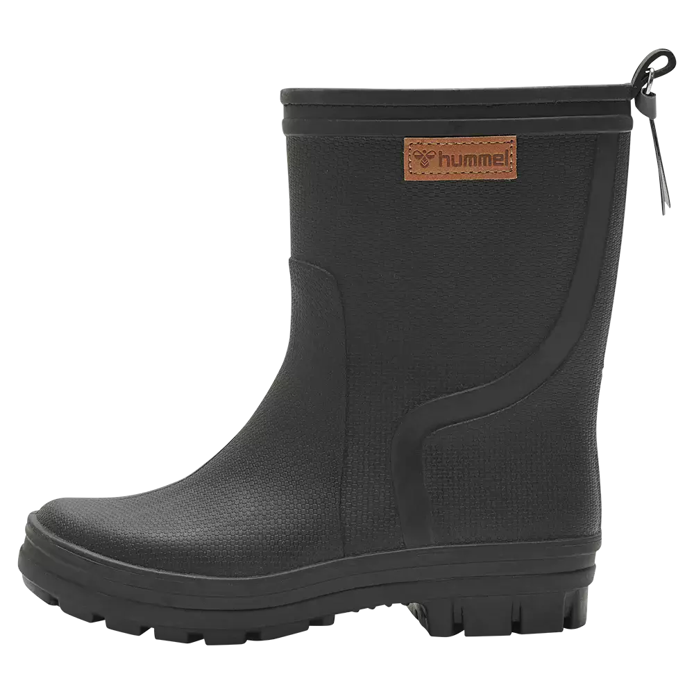 Billedet viser en sort, kort gummistøvle med en robust sål og dybe mønstre for godt greb. Støvlen har en let tekstureret overflade, en dekorativ syning og et lille læder-logo med mærket "hummel" på skaftet. En elastisk kant og en lille træksnøre i toppen gør den nem at tage på. Simpel, funktionel og velegnet til våde, mudrede forhold.