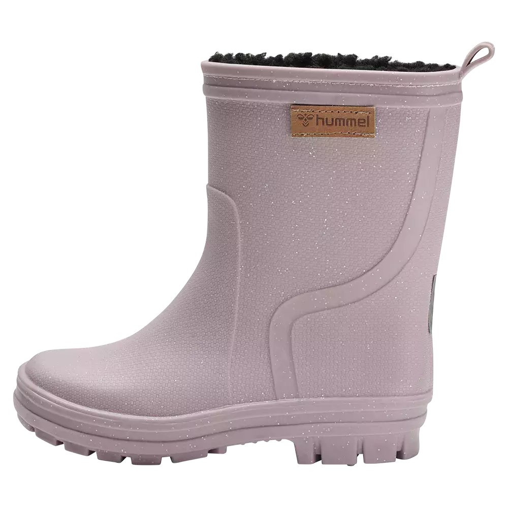 En lys rosa gummistøvle fra Hummel med kort skaft, glitrende finish og blød mørk foring. Støvlen har diskret tekstur i materialet, en praktisk trækhank bagtil og et lille lædermærke med logo på ydersiden. Den robuste, mønstrede sål giver godt greb, og designet er både funktionelt og legende — perfekt til regnvejr og mudrede udendørseventyr for børn.