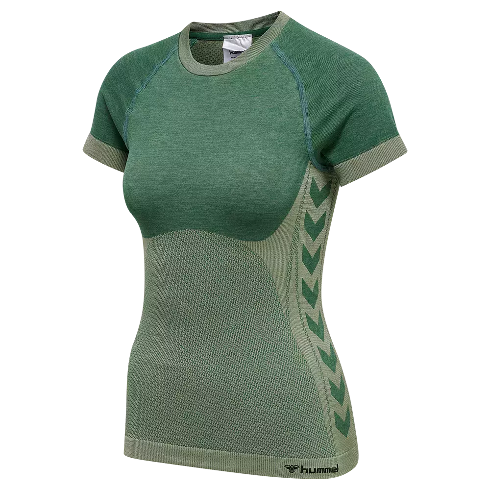 En tætsiddende, kortærmet trænings‑t‑shirt i forskellige nuancer af grønt. Overdelen er glatstrikket, mens maven har et åndbart, mesh‑lignende mønster for ventilation. Siderne prydes af hummels karakteristiske chevron‑mønster, og ribkanter ved ærmer og bund giver et pænt finish. Designet fremstår funktionelt og feminint med formgivende sømme og en sportslig, stilren æstetik egnet til træning og fritid.