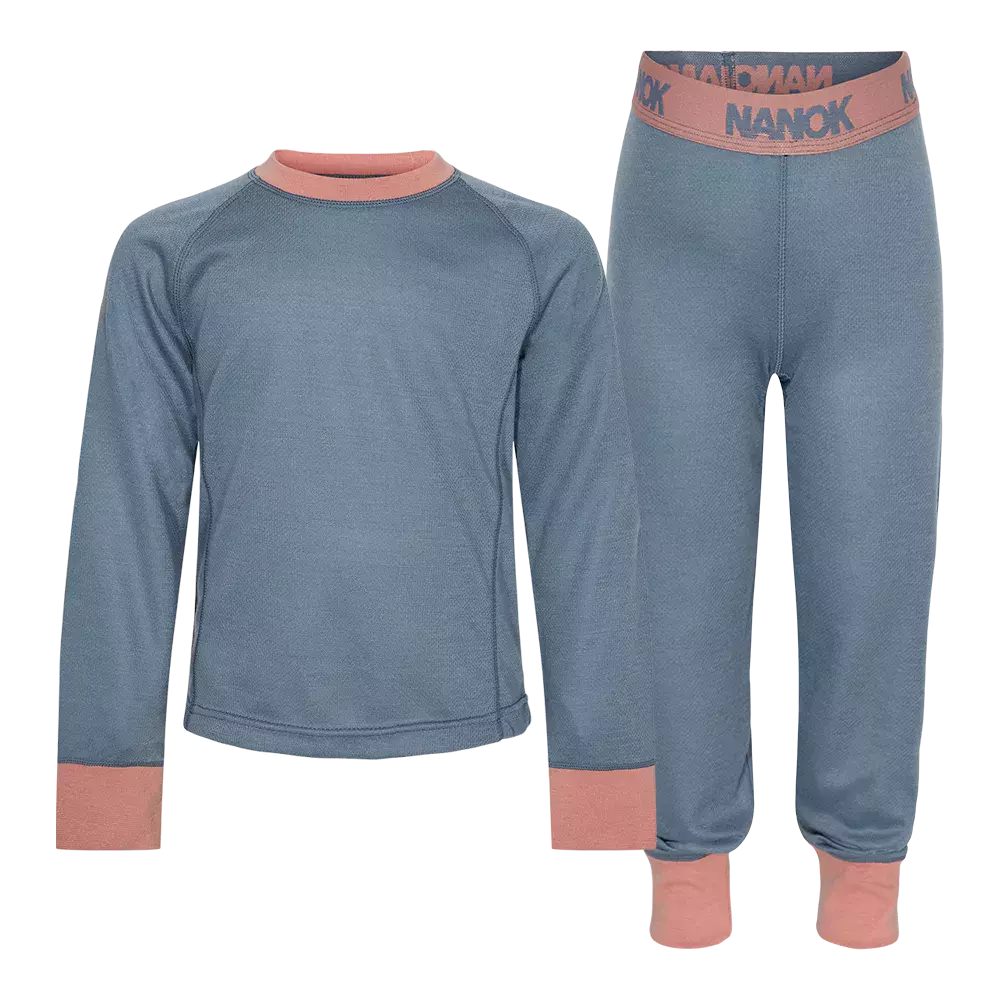 Sæt består af bluse og underbukser/leggings i støvet blå med lyserøde kantdetaljer ved hals, manchetter og talje. Ribbede linninger, tætsiddende snit og elastisk linning med "NANOK"-tryk. Materialet ser ud til at være varmt og strækbart, velegnet som baselag til udendørsaktiviteter i koldt vejr. Enkel, funktionel og komfortabel stil til børn. Let at bevæge sig i.
