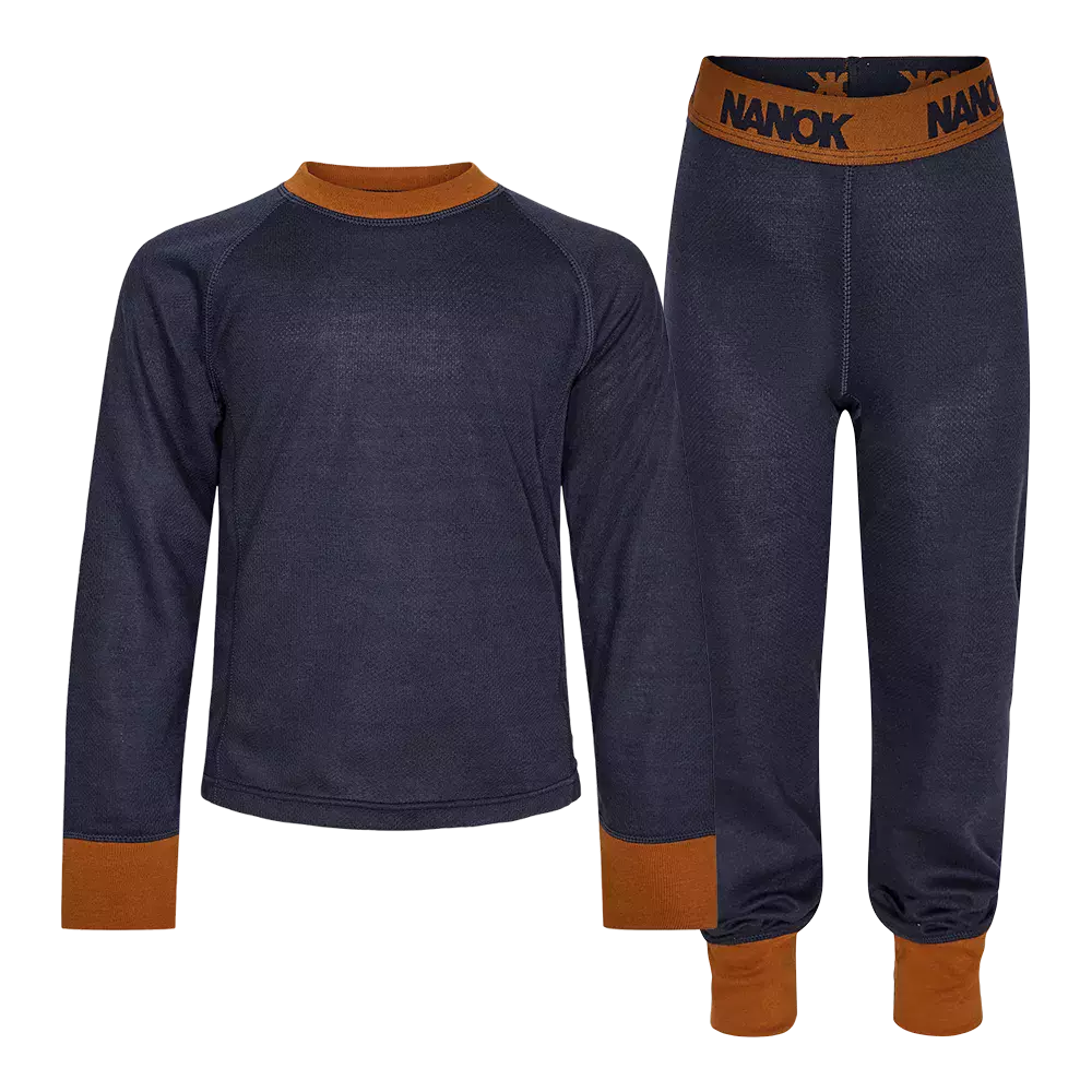 Dette er et todelt undertøjssæt i mørkeblå med varme cognacfarvede detaljer. Sættet består af en langærmet bluse og tætsiddende underbukser med elastiklinning mærket "NANOK". Ribkanter ved hals, håndled og ankler giver god pasform, mens det tætte, fleece-agtige materiale ser isolerende og svedtransporterende ud. Designet virker praktisk til udendørsaktiviteter og kolde dage som et funktionelt og komfortabelt lag under ydertøj.