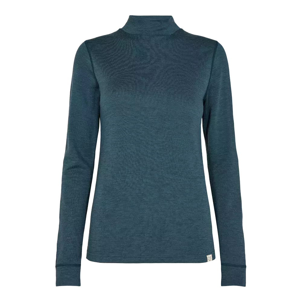 En enkel, tætsiddende langærmet bluse i dyb petrolblå med let meleret struktur. Toppen har høj, kort krave (mockneck) og lange ærmer med brede manchetter, hvilket giver et klassisk, minimalistisk udtryk. Stoffet ser blødt og varmeisolerende ud, egnet til lag-på-lag om efteråret eller vinteren. Perfekt til hverdag eller under en jakke til mere formelle looks.