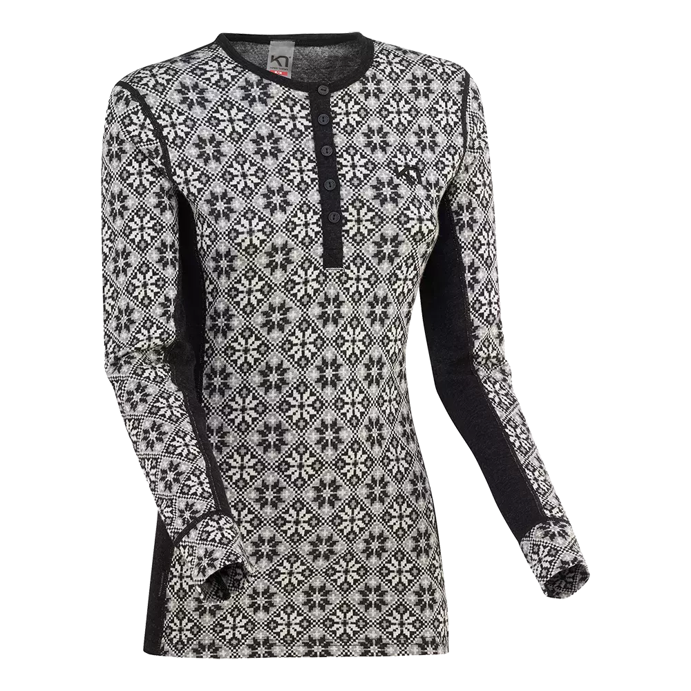 Langærmet, tætsiddende trøje i sort og hvidt med et klassisk nordisk mønster af tern og snefnugslignende stjerner. Modellen har en kort knaplukning ved halsen (henley), kontrastpaneler i sort langs sider og inderærmer samt rullemanchetter. Materialet virker tyndt men isolerende — ideel som baselag under ydertøj eller som varm hverdagsbluse til kolde dage.