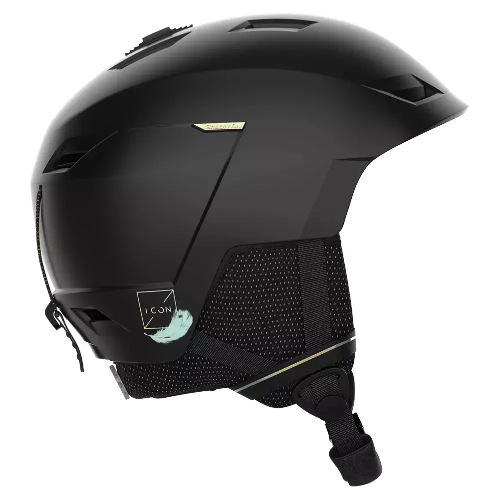 En stilren mat sort skihjelm set fra siden, med aerodynamisk form og flere ventiler i toppen og fronten for god luftcirkulation. Hjelmen har polstrede ørekopper med åndbart mesh, justerbar hakestrop og et lille dekorativt "ICON"-mærke med en lys fjer. Designet virker robust og moderne, velegnet til alpine aktiviteter, hvor sikkerhed, komfort og minimalistisk æstetik er i fokus.