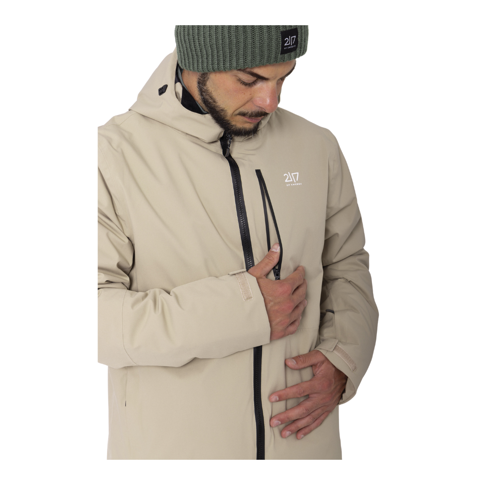 2117 of Sweden præsenterer Kabo Padded Ski Jacket, en funktionel herre skijakke designet til koldere vejr. Jakken fremstår i en klassisk beige farve og er udstyret med en central vandafvisende lynlås. Den har også en justerbar hætte, der sikrer optimal beskyttelse mod vind og vejr. Jakken kombinerer stil med funktionalitet, hvilket gør den perfekt til både ski og daglig brug i vintersæsonen.