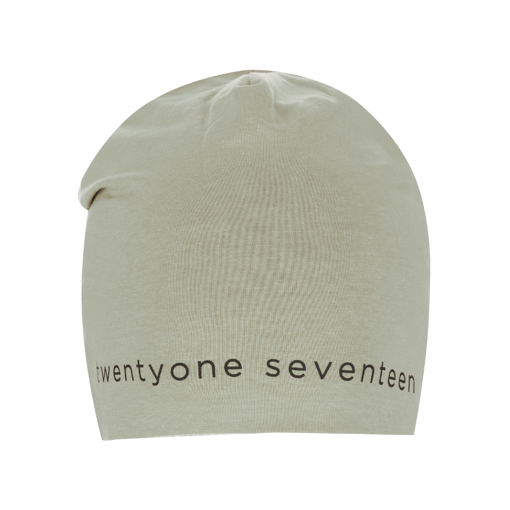 En enkel, lysegrøn/beige strikhue med et blødt, elastisk snit og let slouchy pasform. Langs nederkanten ses trykket 'twenty one seventeen' i enkle, sorte bogstaver, hvilket giver et minimalistisk og moderne udtryk. Huen virker lavet af fint ribstrikket stof, ideel til hverdagsbrug og køligere vejr. Den neutrale farve og rene typografi gør den nem at kombinere med jakker og afslappede outfits.