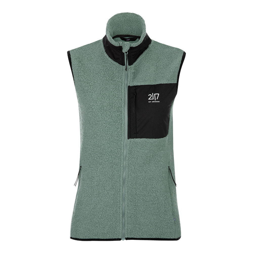 En ærmeløs fleecevest i grønt sherpa-materiale med høj krave og hel lynlås. Vesten har sorte kontrastdetaljer, herunder en brystlomme med lynlås og synligt logo, samt to sidelommer med lynlås. Den bløde, teksturerede overflade giver varme og et afslappet udtryk, perfekt til lag-på-lag om efteråret eller på kølige forårsdage. Enkel, funktionel og velegnet til både hverdag og let friluftsliv.