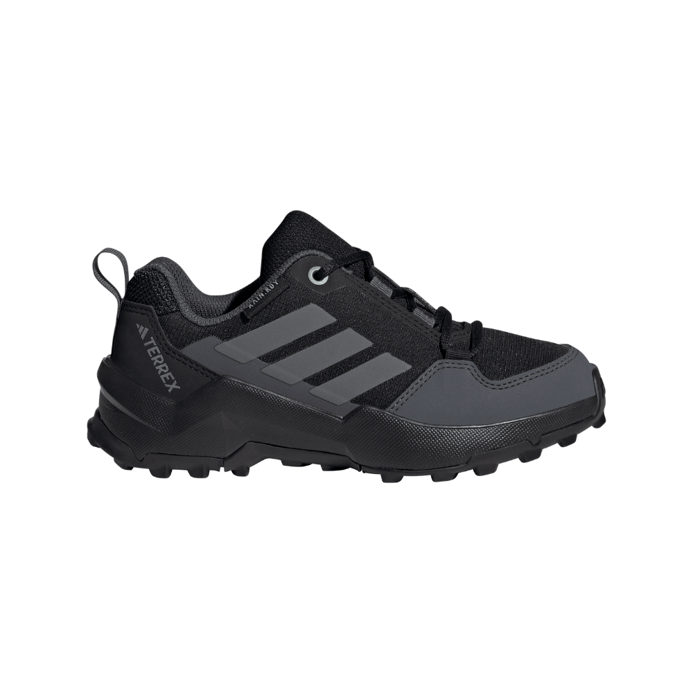 Et lavtstående, robust trail-løbesko i mørkegrå og sort med et funktionelt, minimalistisk design. Skoen har forstærkede paneler ved tå og hæl, åndbart mesh, polstret krave og klassiske tre striber langs siden. Aggressivt mønstret ydersål sikrer greb på ujævnt underlag, mens snørelukning og en bageste trækkestrop giver stabil pasform og praktisk påtagning. Branding 'Terrex' signalerer terrænorienteret design og holdbarhed.
