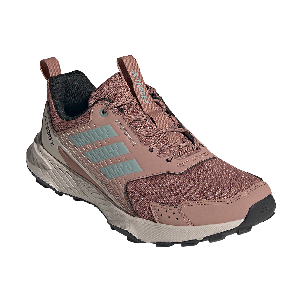 Rosa løbesko fra Adidas Terrex-serien med tydelige lyseblå tre striber og robuste detaljer. Skoen har et ventilerende mesh-overdel, forstærkede syninger og syntetiske overlays ved tå og sider for ekstra holdbarhed. Polstret krave og trækflap ved hælen gør den nem at tage på, mens den profilerede ydersål og affjedrende mellemsål sikrer godt greb og komfort på ujævnt terræn. Funktionel og stilfuld til outdoor-brug.