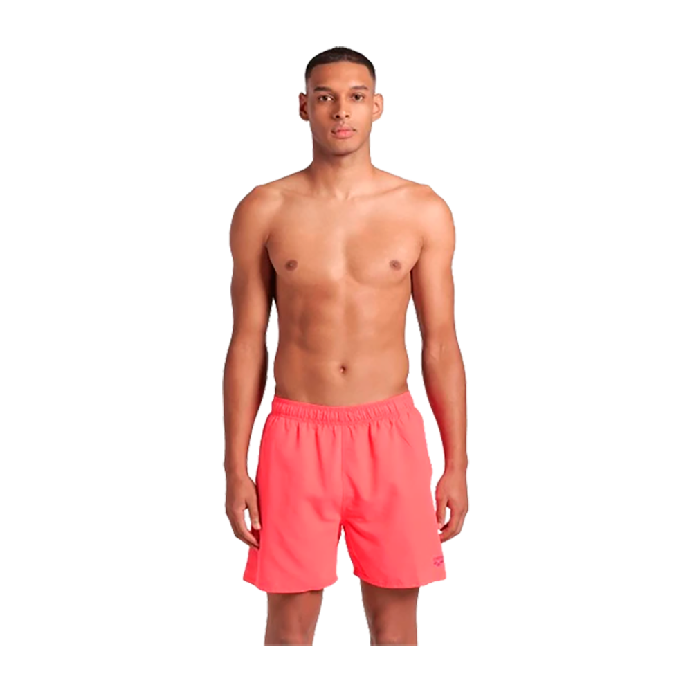 På billedet står en mand frontalt i afslappet positur med bar overkrop og korte, koralrøde badebukser. Badebukserne har elastisk talje og slutter midt på låret, med et enkelt, ensfarvet design. Modellen har kort hår og holder armene afslappet ned langs siderne. Baggrunden er neutral, hvilket fremhæver det rene, minimalistiske look og fokus på badetøjet.