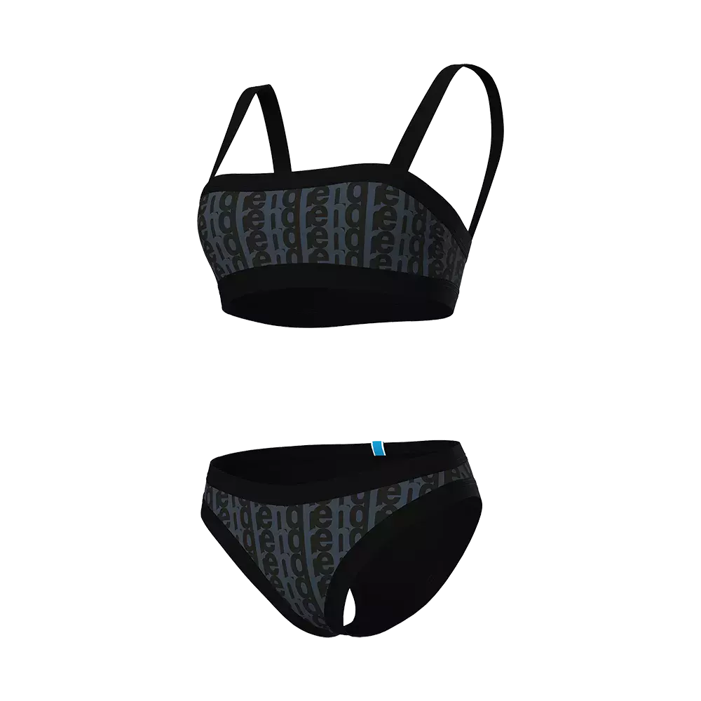 Sort to-delt undertøjsset bestående af en enkel sports-bh med brede stropper og en matchende trusse. Stoffet har et diskret, gentaget bogstavsmønster i mørkegrå toner og en mat, elastisk kant for god støtte. Designet virker minimalistisk og funktionelt med bløde syninger og strækbart materiale. En lille blå etikette på trussen giver et enkelt farveaccent. Settet signalerer komfort og hverdagslig anvendelighed.