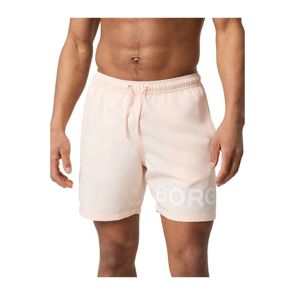 Billedet viser en mandlig overkrop og ben iført lyserøde, knælange badeshorts med elastisk talje og snøre. Shortsene har en diskret sidesøm og et stort, hvidt "BORG"-logo på låret. Stoffet ser let og hurtigtørrende ud, velegnet til strand eller træning. Modellen står afslappet med hænderne langs siden, hvilket fremhæver det enkle, sporty og moderne design.