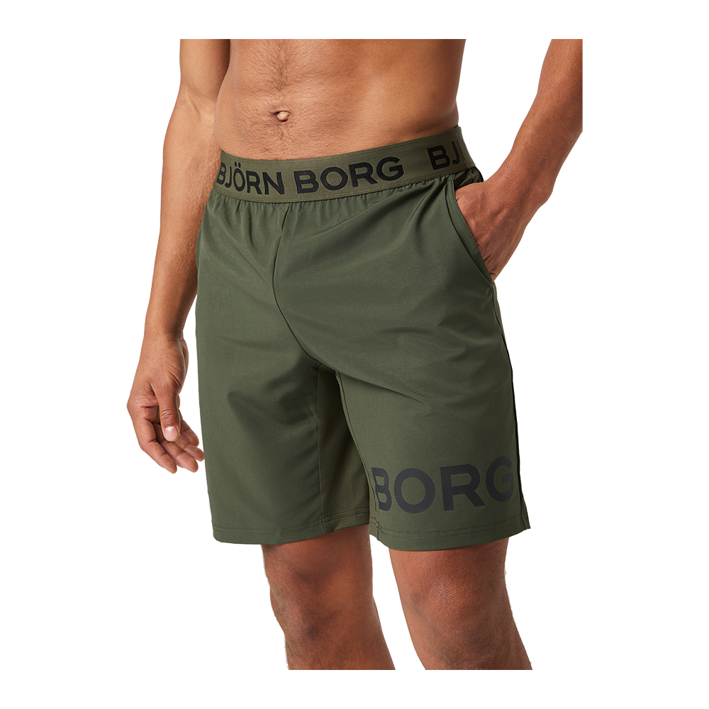 Et nærbillede viser en mandlig model iført olivengrønne træningsshorts fra mærket Björn Borg. Shortsene har elastisk taljebånd med stort logo, sidelommer og et afslappet fit, der når midt på låret. Stoffet ser let og teknisk ud, egnet til sport eller fritid. Farven og det minimalistiske design giver et moderne, funktionelt udtryk, velegnet til både træning og hverdagsbrug.