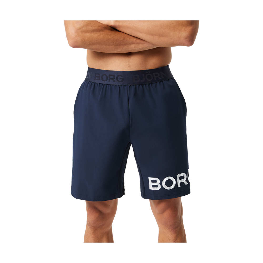 Et par mørkeblå træningsshorts i midt-længde med en elastisk linning, der bærer teksten "BJÖRN BORG". Shortsen har en afslappet pasform til bevægelse og et stort hvidt logo "BORG" langs venstre lår. Materialet fremstår let og funktionelt, velegnet til både træning og afslappet brug, med et enkelt og moderne sportsligt design.