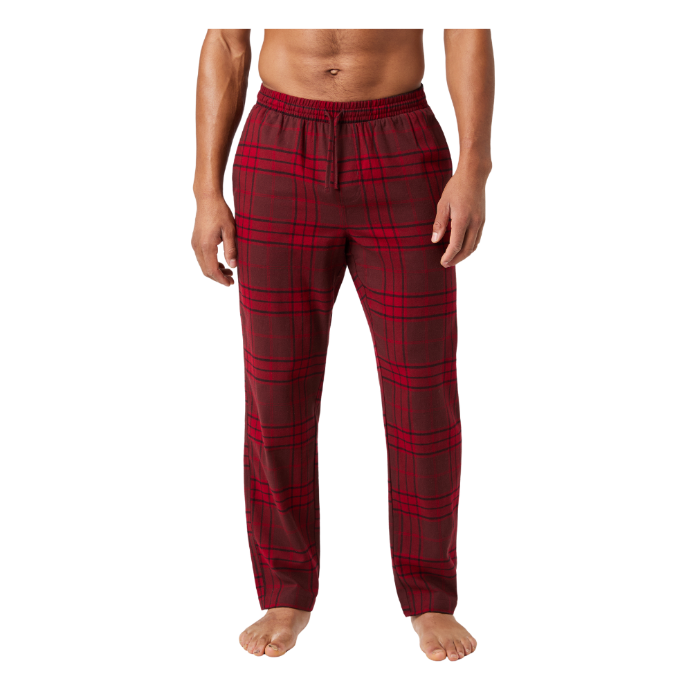 Et par røde, ternede pyjamasbukser i blødt materiale ses på en person stående barfodet. Bukserne har en elastisk talje med snøre og en afslappet, lige pasform, som giver god bevægelsesfrihed. Det klassiske tartanmønster og varme farvenuancer giver et hyggeligt, hjemligt udtryk, velegnet til afslapning eller nattetid. Bukserne fremstår komfortable og casual.