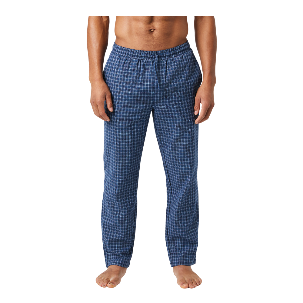 En mand står afslappet iført blåternet pyjamassbukser med elastisk talje. Billedet viser kun kroppen fra navlen og ned til fødderne, så ansigtet ikke er synligt. Bukserne har et klassisk, ternet mønster i forskellige blå nuancer og et løst, behageligt fit, der egner sig til afslapning hjemme. Han står barfodet på en neutral baggrund, hvilket fremhæver et enkelt, hverdagsagtigt udtryk.