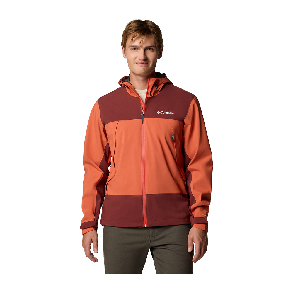 En ung mand står afslappet foran en neutral baggrund iført en tofarvet Columbia-ytterjakke i varme orange og burgunderrøde nuancer. Jakken har hætte, sømmer, lynlås foran og lynlåslommer, hvilket giver et funktionelt, udendørspræget udtryk. Han bærer også mørkegrønne bukser og har et roligt, venligt ansigtsudtryk. Hele fremtoningen virker praktisk og moderne, egnet til vandreture eller hverdagens friluftsaktiviteter.
