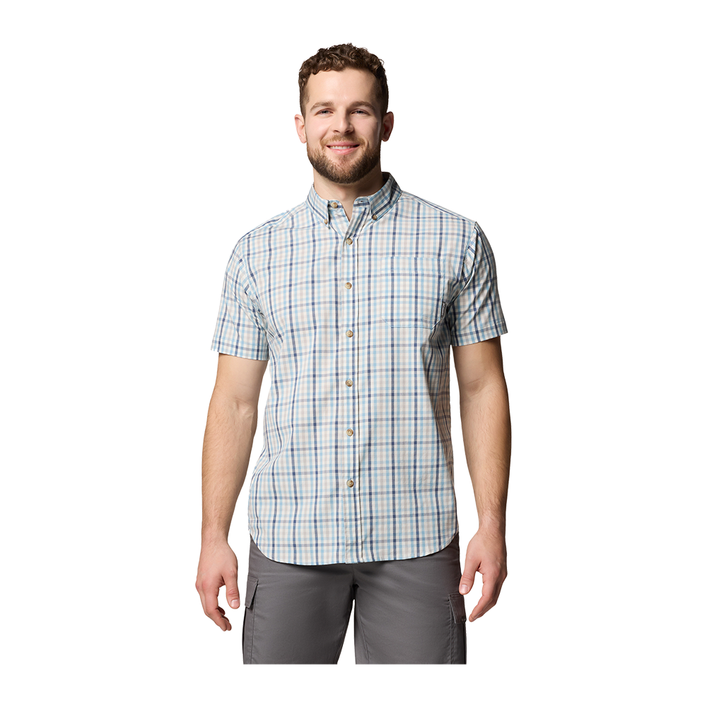 En smilende, velsoigneret mand står afslappet mod en neutral baggrund iført en kortærmet, lyseblå og beige ternet skjorte med knapper og grå cargobukser. Skjorten er knaplukket til halsen og giver et casual, sommerligt udtryk, mens de praktiske lommer på bukserne antyder funktionalitet. Hans afslappede holdning og venlige ansigtsudtryk skaber et imødekommende og hverdagsagtigt look.