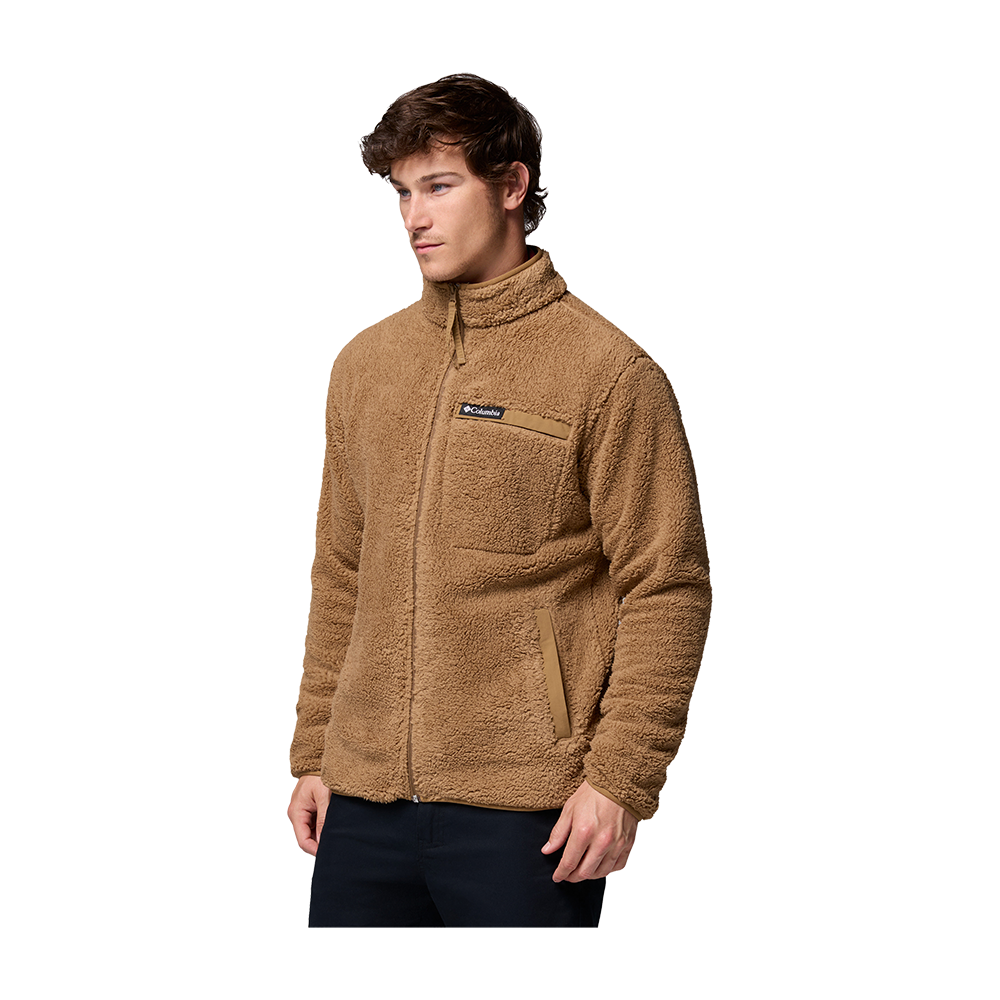 En ung mand iført en varm, karamelbrun teddy-fleecejakke med fuld lynlås og høj krave. Jakken har en synlig brystlomme med logo og to skrå sidelommer, og materialet fremstår blødt og fyldigt. Modellen står i afslappet positur, kigger let til siden med hænderne ned langs kroppen. Billedet fremhæver jakken som et komfortabelt og praktisk valg til kolde dage.