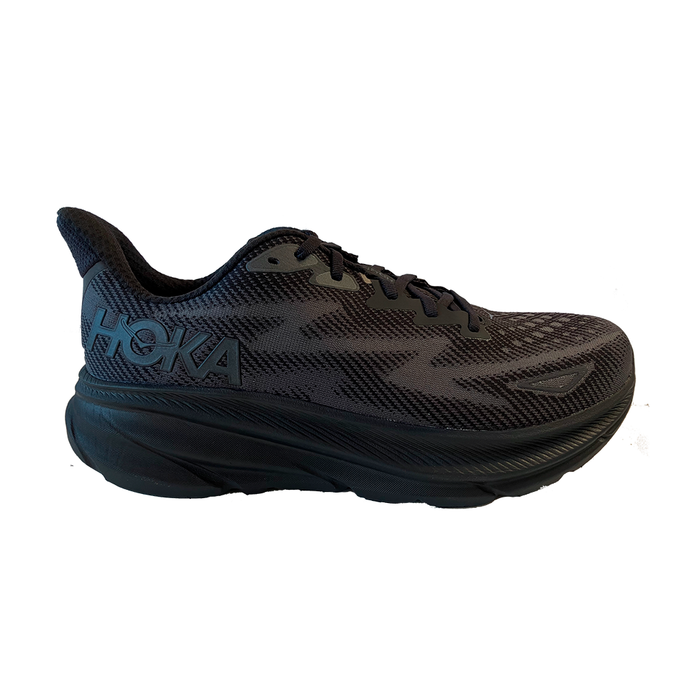 Et foto af en sort Hoka løbesko med kraftig, polstret mellemsål og tekstureret mesh-overdel. Skoen har sorte snørebånd, diskret logo på siden og et buet design for øget dæmpning og fremdrift. Den brede sål antyder stabilitet og komfort til lange distancer, mens det åndbare materiale giver ventilation. Stilen er moderne og minimalistisk, velegnet til både træning og hverdagsbrug.