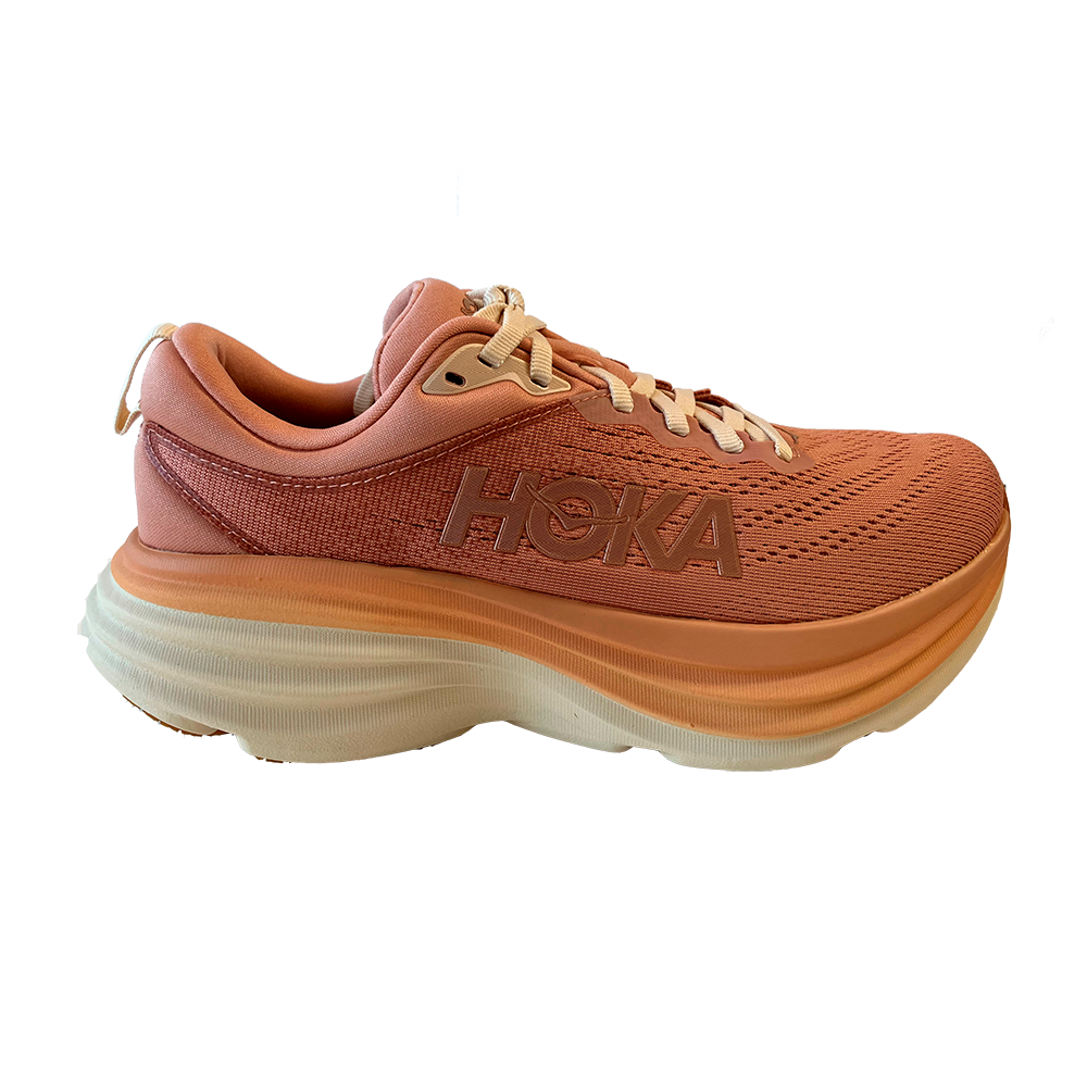Et koralfarvet Hoka-løbesko ses fra siden med kraftig, ekstra polstret sål i lag af orange og creme. Overdelen er i åndbar mesh med fine syninger og HOKA-logoet trykt på siden. Skoen har flade beige snørebånd, blød hælkappe og et let, affjedrende design, der signalerer komfort og stabilitet til lange løbeture eller hverdagsbrug.