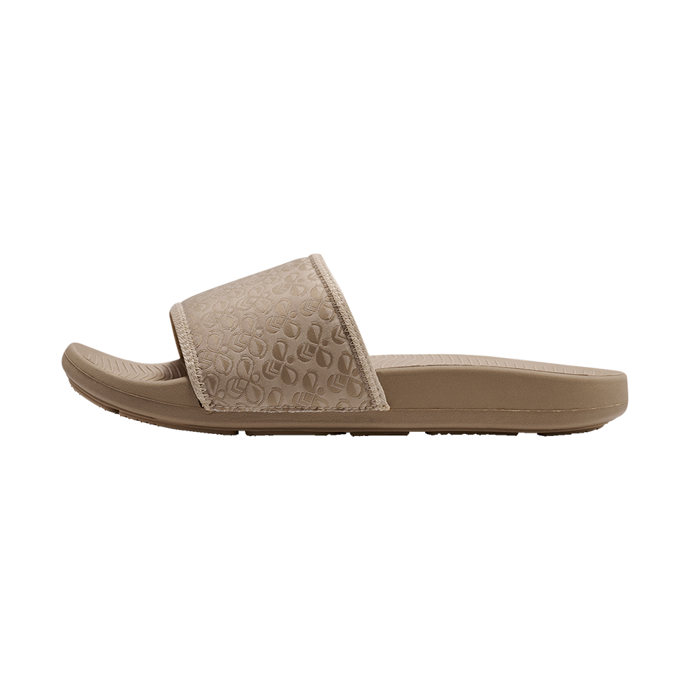 Den beige slidesandal har et enkelt, moderne design med en bred rem dækket af diskrete, præget mønstre i gentagne former. Sålen er anatomisk formet med let vaffelmønster ved tåområdet og en blød, stødabsorberende profil, der lover komfort ved hverdagsbrug. Materialerne virker vandafvisende og lette, hvilket gør sandalen praktisk til stranden, poolen eller afslappede ture i byen.
