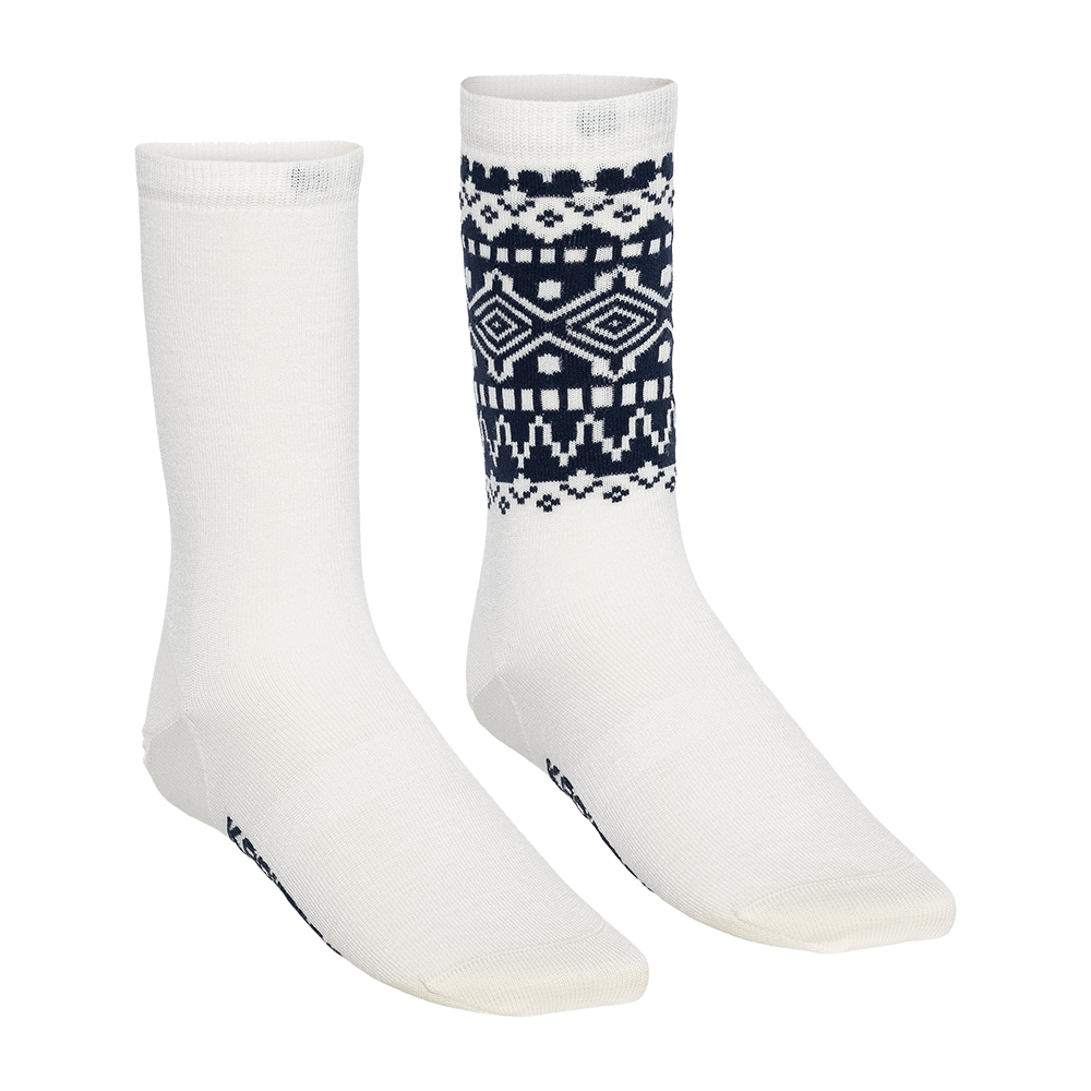 Dette billede viser et par hvide knæstrømper i mellemlang længde, hvor den ene strømpe er ensfarvet hvid og den anden har et dekorativt mørkeblåt nordisk mønster på skaftet. Stoffet virker blødt og tætstrikket med forstærket tå og hæl. Strømperne fremstår som et stilfuldt, komfortabelt valg til hverdagsbrug eller kolde dage, kombineret med både afslappet og mere formelt tøj.