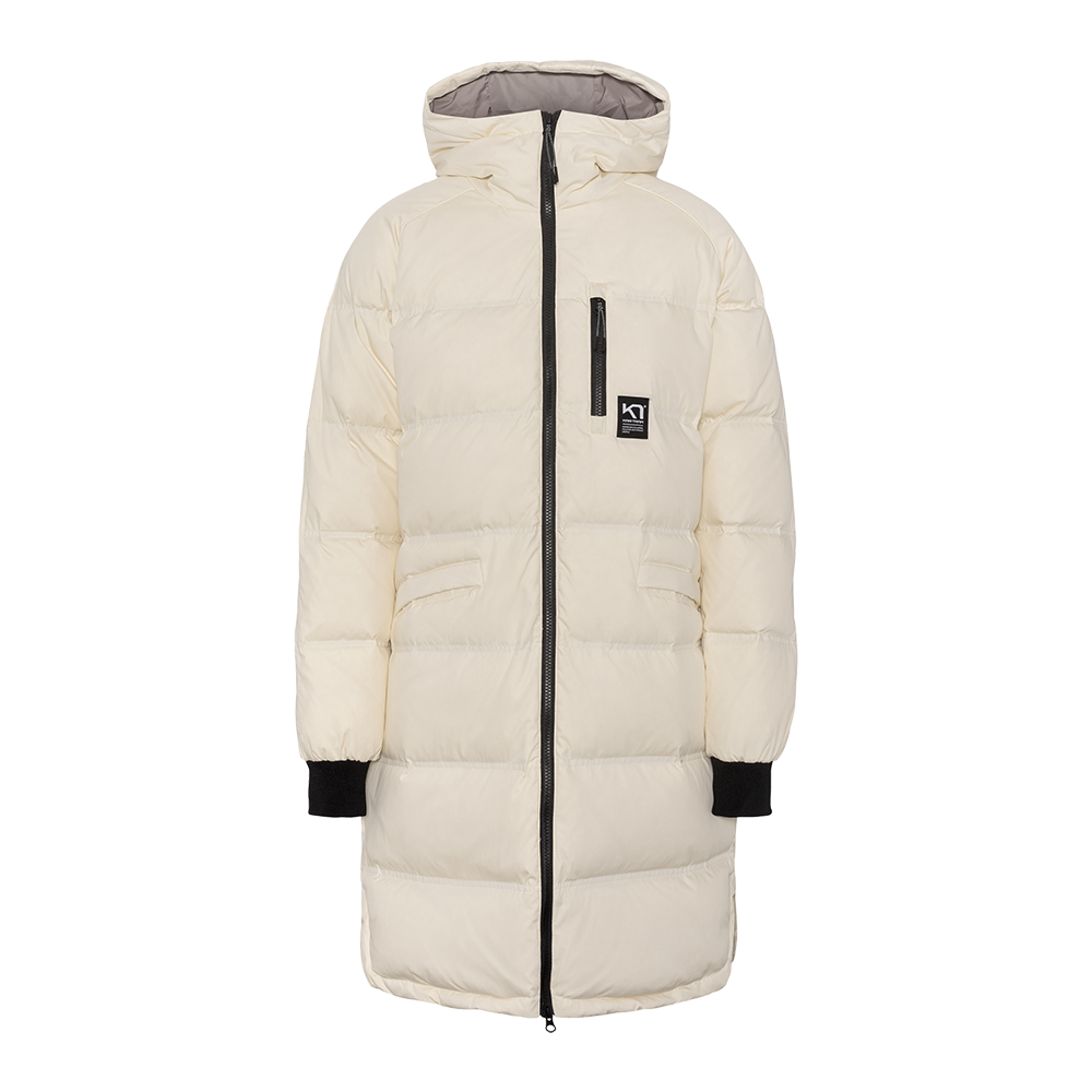 En lang, vatteret vinterfrakke i varm cremehvid med en høj hætte og nedre længde, der dækker lårene. Jakken har brede vandrette quiltede felter, en kontrastgivende sort tovejs-lynlås og sorte ribkantede ærmegab. Praktiske detaljer inkluderer en lodret brystlomme med lynlås, skrå sidelommer og et lille logo på brystet. Stilren og funktionel med fokus på varme og bevægelsesfrihed.