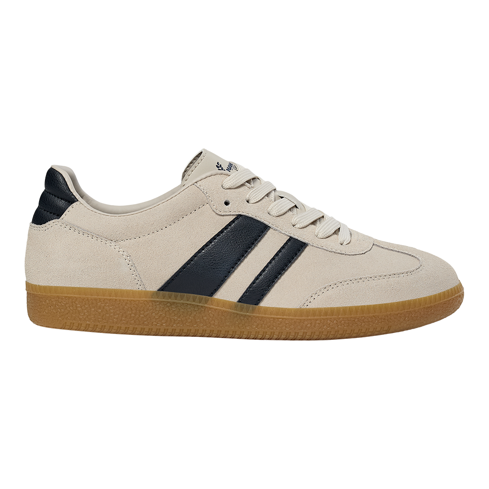 En lav, klassisk sneaker i lyst beige ruskind med to mørkeblå striber langs siden og matchende hælkappe. Skoen har flade, hvide snørebånd, dekorative syninger og en gennemskinnelig, lysebrun gummisål med tekstureret mønster. Den enkle, retroinspirerede silhuet giver et tidløst, afslappet udtryk, velegnet til både hverdag og fritid, og kombinerer komfort med et stilrent, sporty look.