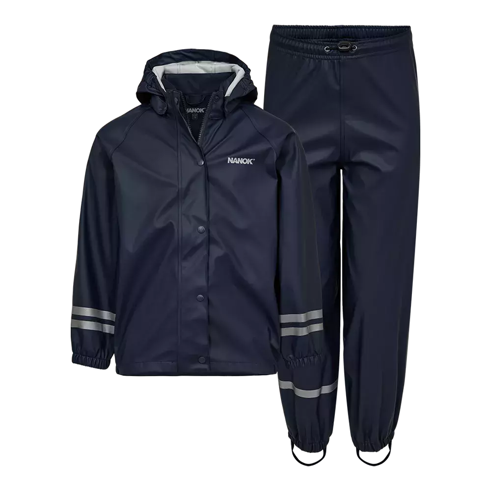 Dette mørkeblå regnsæt består af en vandtæt jakke med hætte og matchende bukser med et diskret NANOK-logo. Jakken lukkes med trykknapper og har elastiske ærmegab, mens bukserne har elastisk talje, fodstropper og forstærkede sømme. Reflekterende striber på ærmer og bukseben øger synligheden i mørke. Sættet fremstår praktisk og robust, velegnet til regnvejr og udendørs leg.