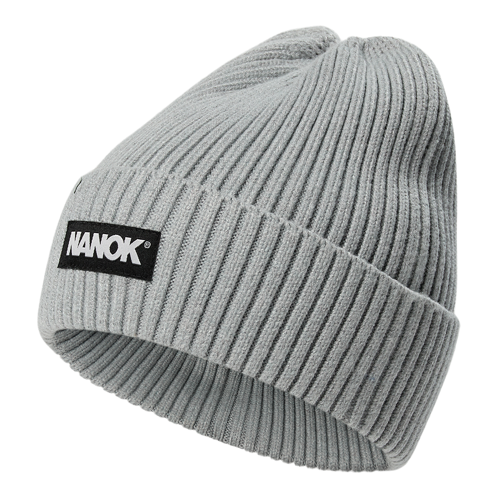 En lysegrå, ribstrikket hue med foldet kant og tæt, blød struktur. Huen har et enkelt, tidløst design og et sort mærkelabel med hvid teksten 'NANOK' foran, som giver et stilrent kontrastelement. Materialet ser varmt og fleksibelt ud, velegnet til kolde dage og hverdagsbrug. Enkel og funktionel, nem at style til både jakker og casual overtøj.