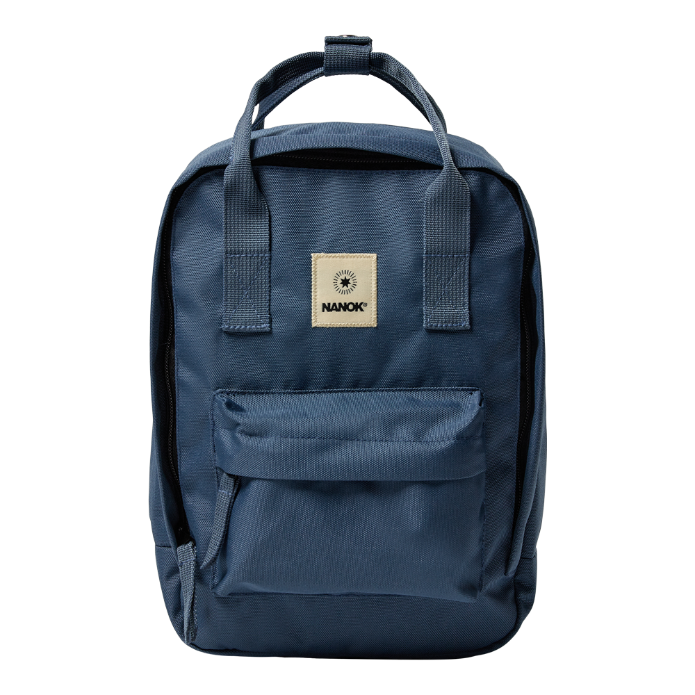 Blå rygsæk i robust, vævet stof med en enkel, firkantet form. Den har polstrede bærehåndtag øverst, brede skulderstropper og en frontlomme med lynlås. Et lysebrunt logo-patch med navnet "NANOK" sidder centralt på forsiden. Designet er funktionelt og minimalistisk, velegnet til hverdag, skole eller kortere ture, med solid syning og praktisk rummelighed.
