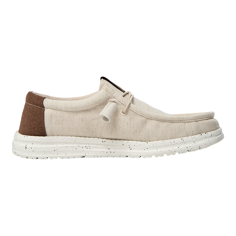 Et lyst, casual lærredssko set fra siden med en enkel, lav profil. Overdelen er beige canvas med synlige syninger og en brun ruskindsforstærkning ved hælen. Skoen har en afslappet moccasinform, korte snørebånd med knude og en tyk, hvid gummisål med sorte prikker, der giver et moderne, råt touch. Perfekt til afslappet hverdag og sommerbrug.