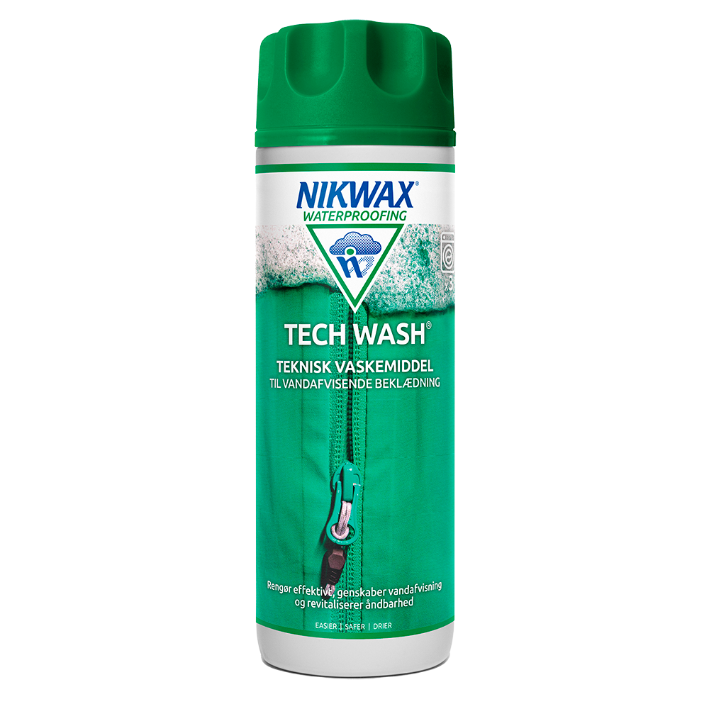 Et billede af en Nikwax Tech Wash-flaske: høj, cylinderformet beholder med grønt låg og tydelig grøn-hvid label. Produktnavn og logo fremgår klart, samt teksten "teknisk vaskemiddel til vandafvisende beklædning". Designet viser en lynlås og skum, der signalerer rengøring og genoplivning af imprægnering. Produktet markedsføres til at rense, genskabe vandafvisning og bevare stofs åndbarhed ved udendørs beklædning.