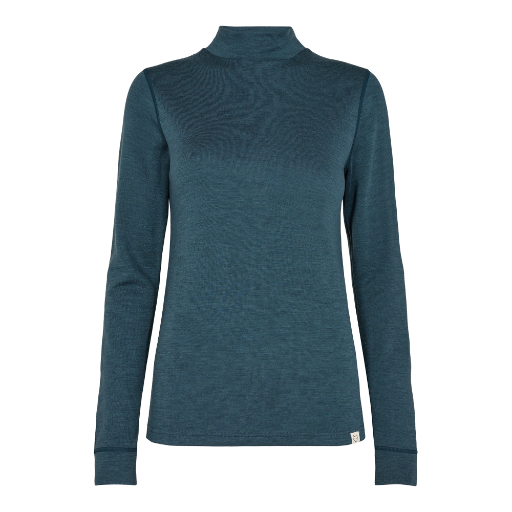 En enkel, tætsiddende højhalset bluse i dyb petrolblå med lange ærmer. Stoffet virker som en fin, let strik eller merinould med en glat overflade, der lægger sig nært kroppen. Designet er minimalistisk med rene sømme og en lille logoetiket ved faldet. Blusen er alsidig til både lag-på-lag og enkel styling, ideel til hverdag eller som basis i garderoben.