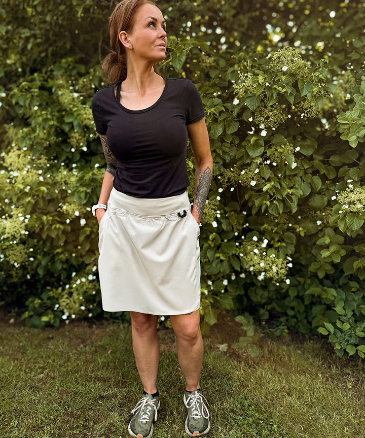 NORD Malene W. er en innovativ nederdel med indbyggede shorts, der er ideel til aktive kvinder. Denne beigefarvede nederdel er designet med en slå-om-effekt og indertights, der tilbyder komfort og beskytter mod irritation, hvilket gør den perfekt til sport eller varme sommerdage. Med en bred elastik i taljen sikres en god pasform, og den har to dybe lommer samt en sikker lynlåslomme, der er ideelle til opbevaring af mindre genstande.