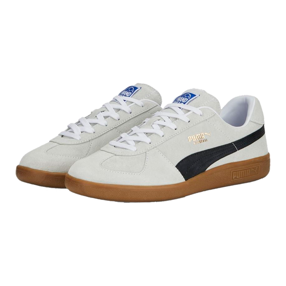 Et par lave Puma-sneakers i lyst gråt ruskind med hvide snørebånd og en kontrastfuld sort formstripe langs siden. Gummisålen i brunlig "gum" giver skoen et retropræg, mens det gyldne Puma-logo og den blå label på tungen tilfører diskrete branddetaljer. Designet er rent og minimalistisk, ideelt til afslappet hverdagsbrug og kombinerer vintage æstetik med moderne komfort.