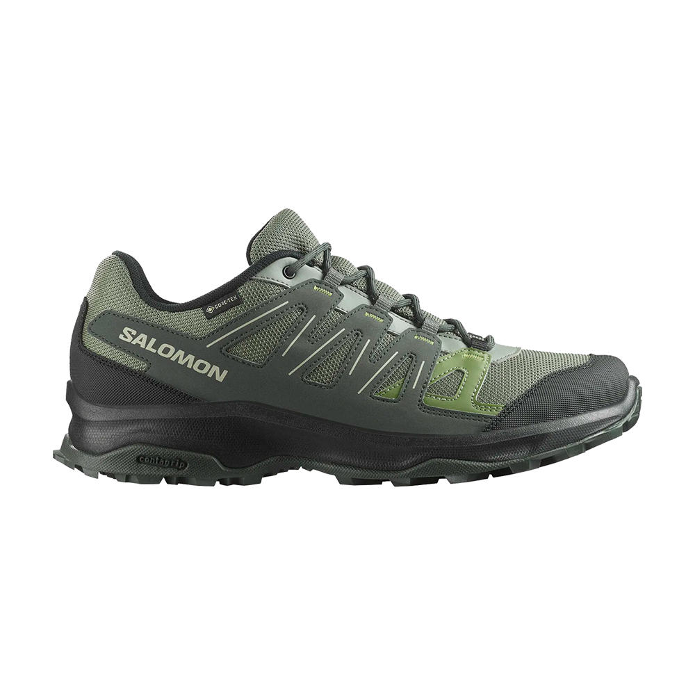 Et grønt-lavgråt, lavt vandresko fra Salomon med tydelig branding på siden. Skoen har mesh-overdel med syntetiske forstærkninger, robust gummisål med dybt mønster og kontureret mellemsål for støtte. Synlig Gore-Tex-label og Contagrip-sål antyder vandtæt, åndbar funktion og godt greb på ujævnt terræn. En praktisk og slidstærk trail-sko designet til lange ture og stabilitet i naturen.