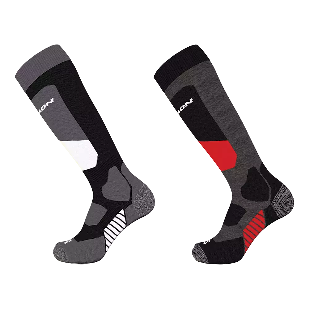 Billedet viser to høje, tekniske sokker i sportstil, placeret side om side mod en hvid baggrund. Sokkerne har asymmetriske farveblokke i grå, sort, hvid og røde detaljer, kraftig forstærkning ved hæl og tå samt ribbet skaft. Designet signalerer komfort og støtte til skidag eller udendørs aktiviteter med polstrede paneler og anatomisk pasform. Farvekontrasterne giver et moderne, dynamisk udtryk.