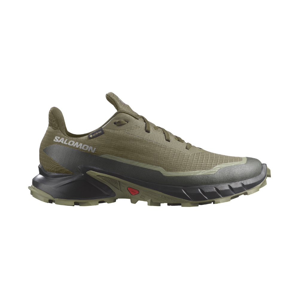 En olivengrøn Salomon trailsko med lavt skaft og robust profil. Den har et åndbart, vandtæt Gore‑Tex-overdel, forstærket tåbeskyttelse og en kraftig, mønstret ydersål til greb på ujævnt terræn. Skoen fremstår let og stabil med polstret hælkappe, synlige snørehuller og solid mellemsål for stødabsorbering — designet til lange ture i naturen og krævende underlag.