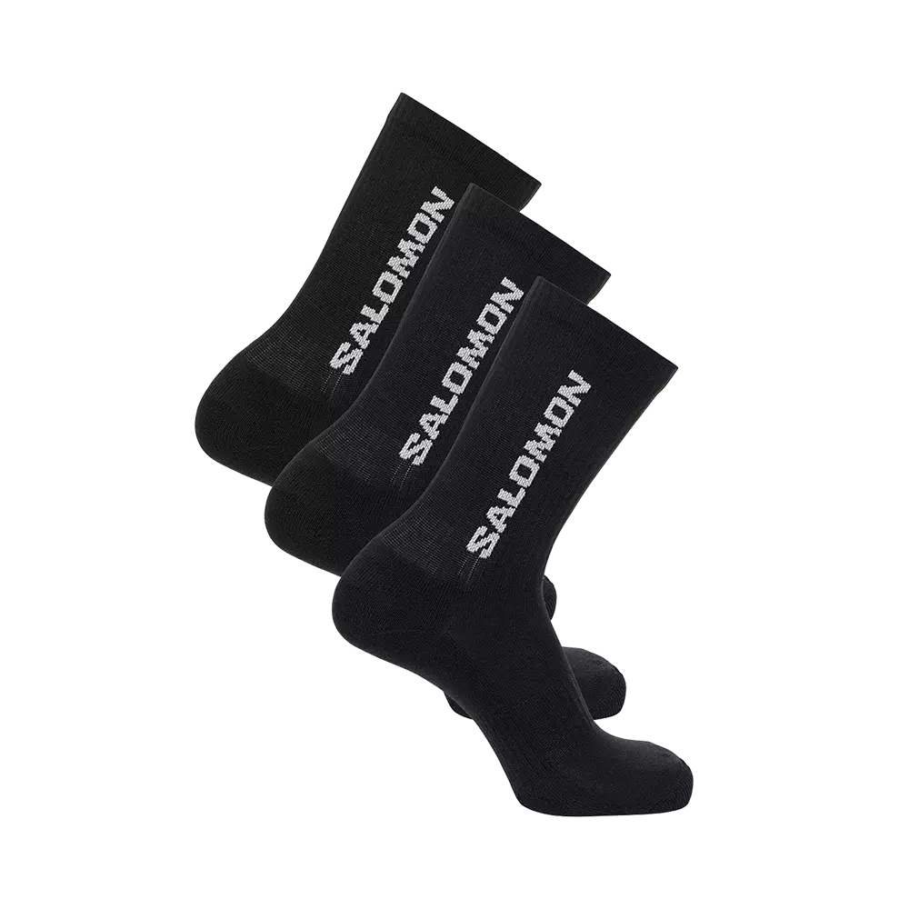 Tre par sorte mellemlange sokker med klart hvidt "SALOMON"-logo langs skaftet. Sokkerne har ribbet skaft og en tætsiddende, anatomisk form der signalerer sport- eller hverdagssokker med støtte omkring hæl og fod. De fremstår med let polstring for ekstra komfort og et klassisk, funktionelt udtryk. Billedet viser dem lagt forskudt ovenpå hinanden i et minimalistisk produktfoto.