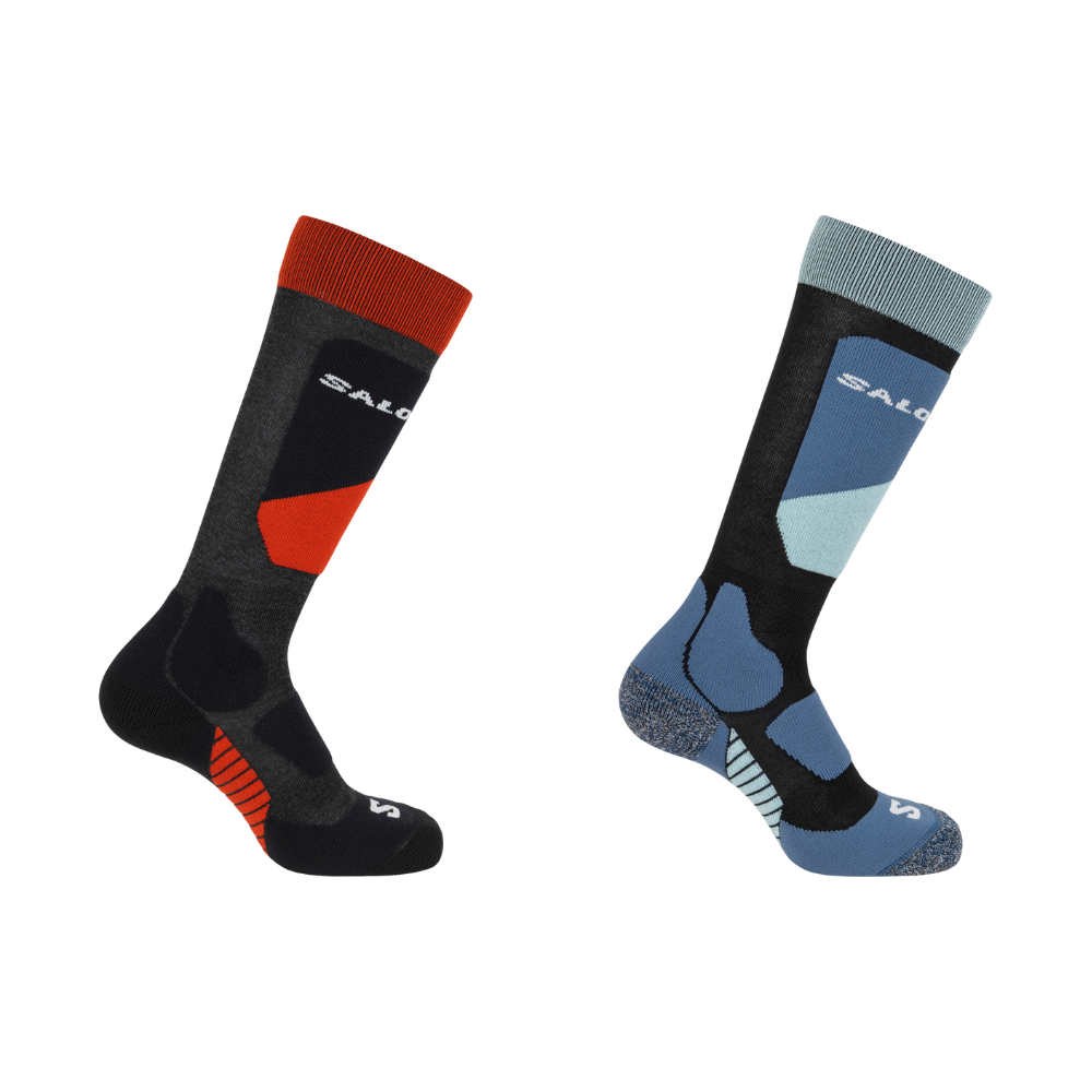 To tekniske skistrømper præsenteres side om side: venstre i mørkegrå og sort med klart orange-rød accent ved skaft og vrist, højre i sort og blå med lyseblå kontrastpaneler. Begge har ribbet skaft, anatomiske polstringer ved hæl og tå, ekstra støtte under fodsålen og slidstærkt materiale. Designet signalerer komfort, varme og stabilitet til aktive vinter- eller udendørsaktiviteter.