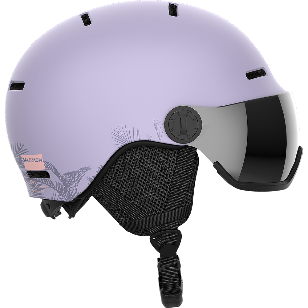 En moderne, sart lyse-lilla skihjelm med indbygget, tonet visir og mat overflade. Hjelmen har ventilationsåbninger i toppen, justerbar rem under hagen og polstrede, sorte mesh-øreklapper for komfort. På bagsiden ses et diskret bladmønster og en lille rosa Salomon-label. Designet fremstår strømlinet og funktionelt, velegnet til både alpint skiløb og snowboard, med fokus på sikkerhed og stil.